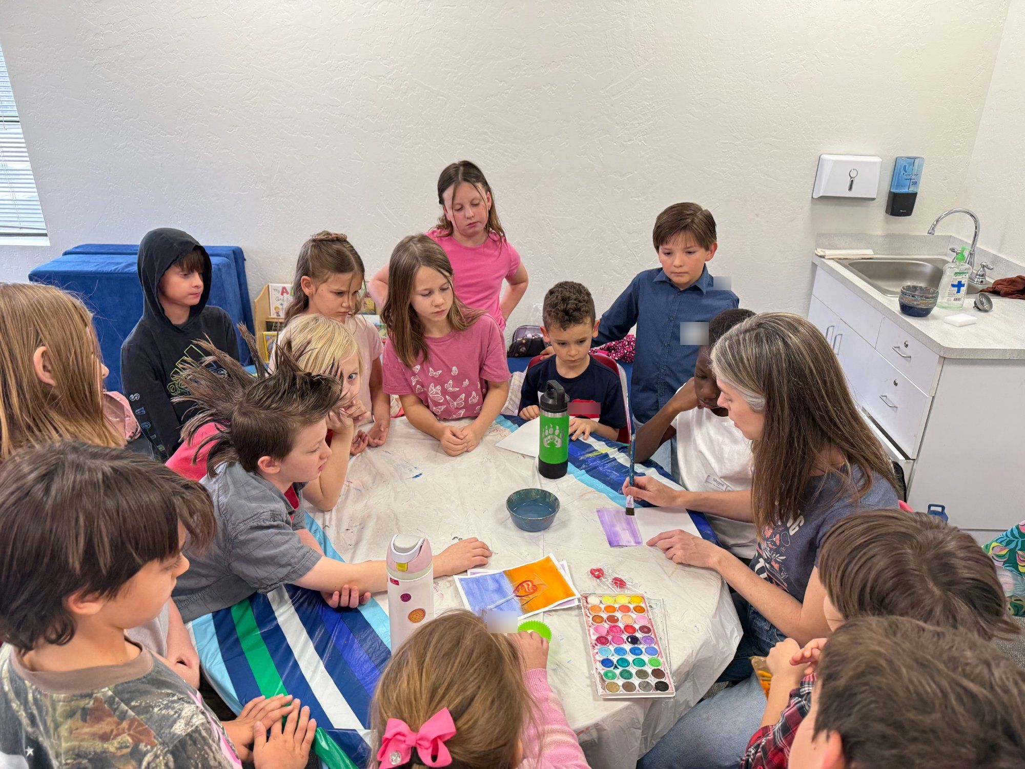 Art teacher with students gathered around watercolor project